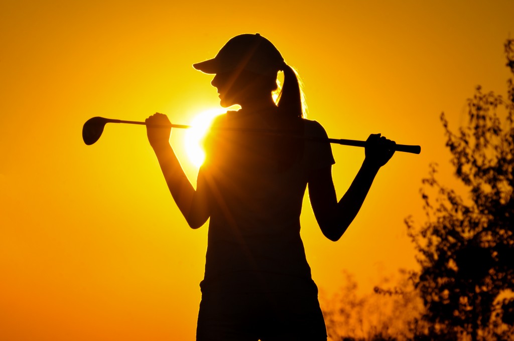 woman golf player tee off during sunset silhouetted